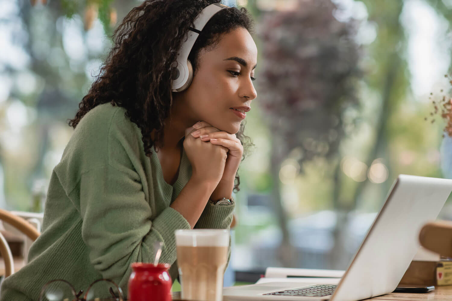A young woman wearing headphones sits at a table with a laptop